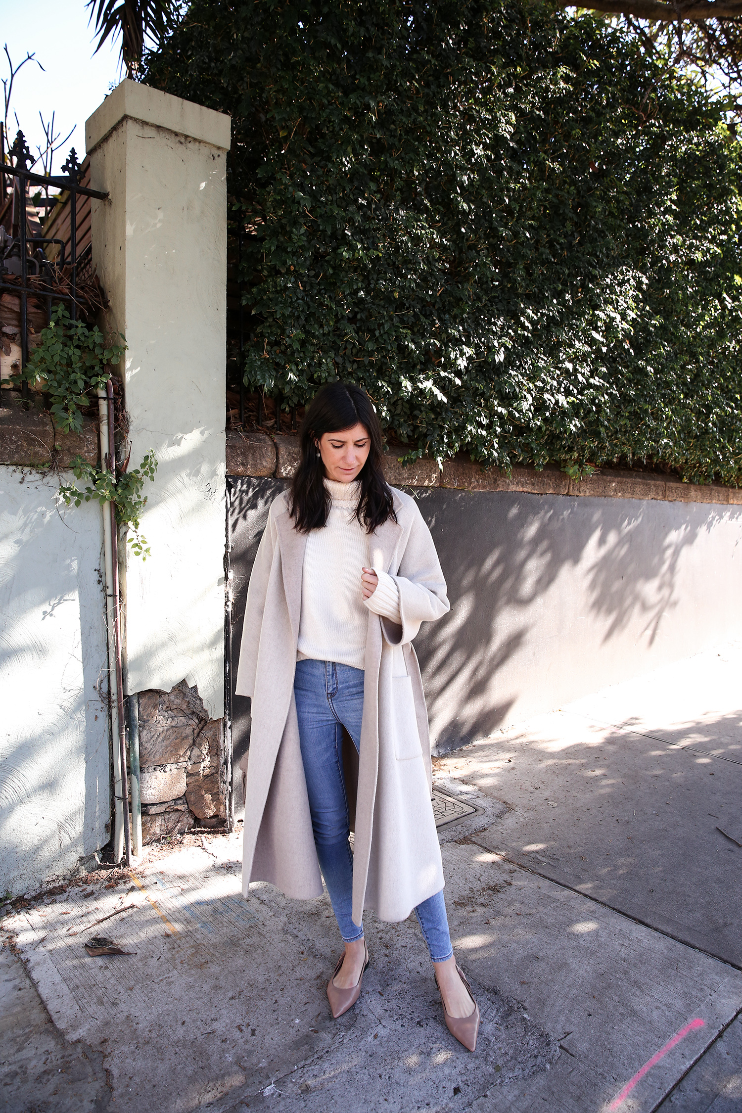 Scandi style outfit wearing white rollneck sweater skinny jeans and a duster coat