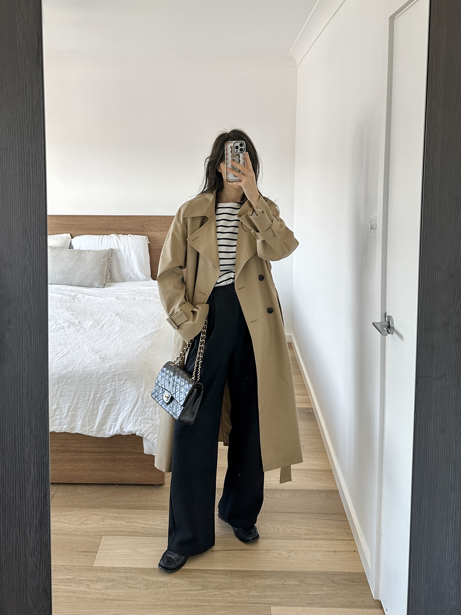 Minimalist French Parisian style outfit wearing stripes black trousers and a trench coat